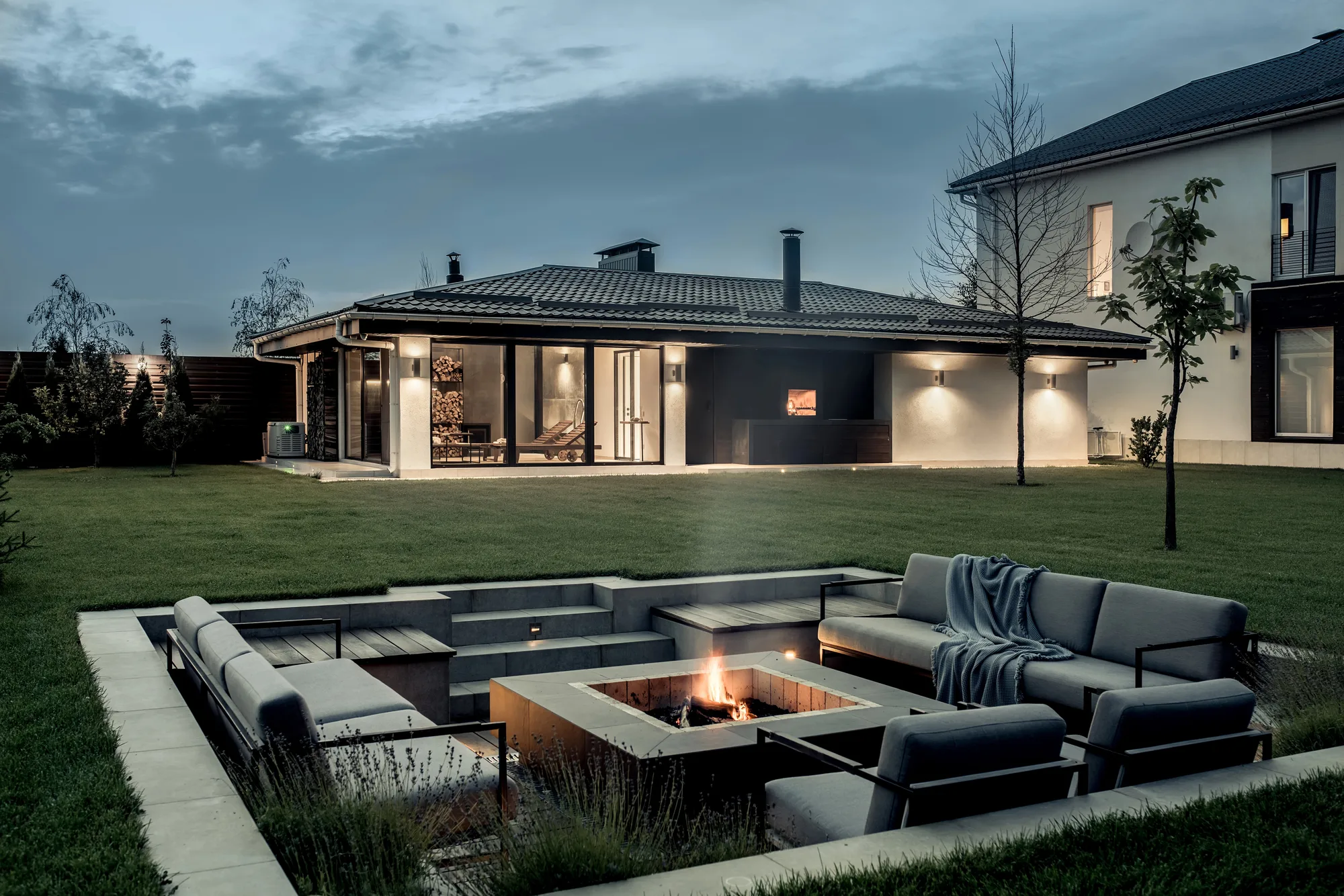 Sunken lounge with built-in seating around a square fire pit beside a home