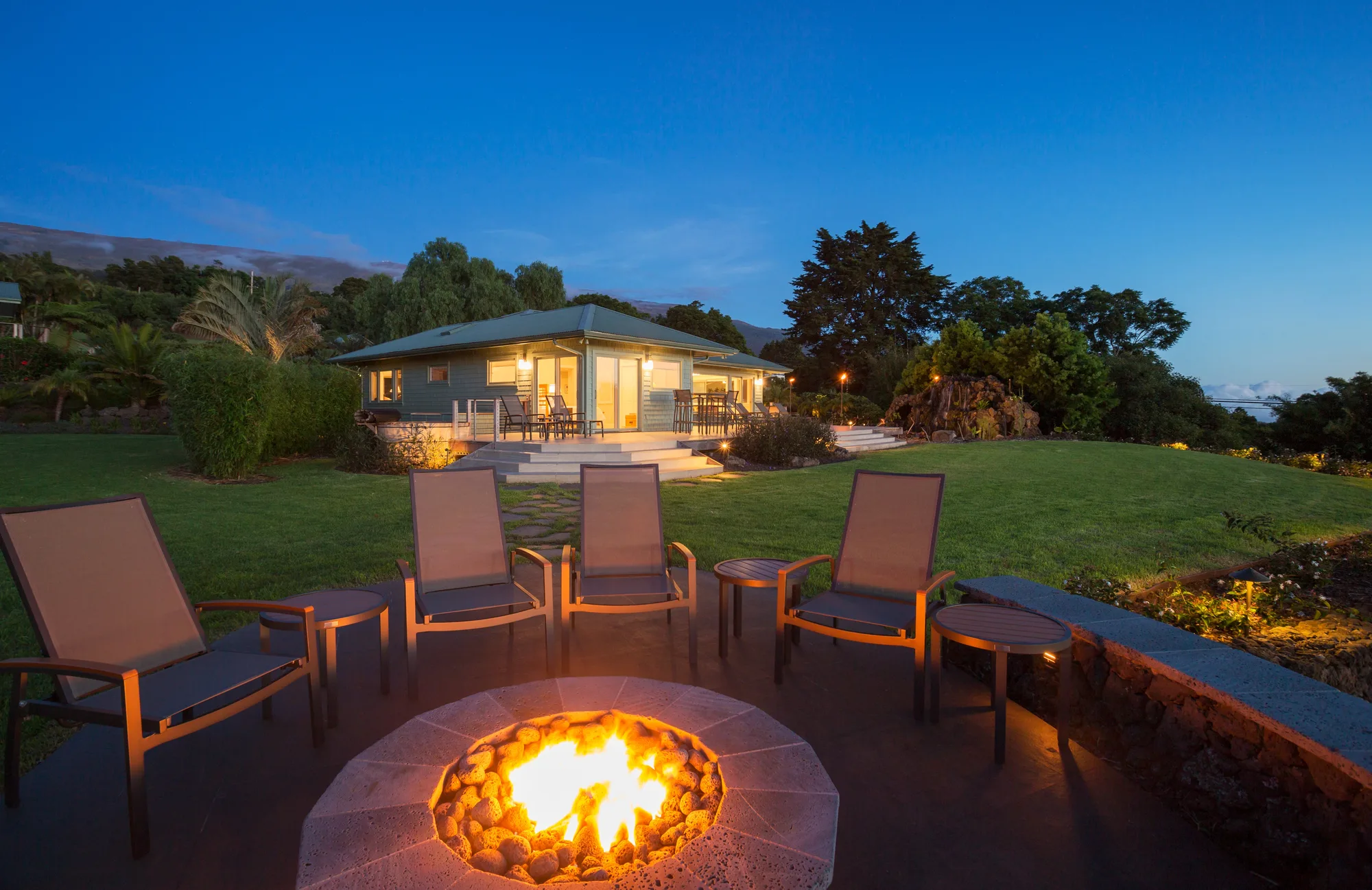 Round gas fire pit with outdoor chairs on a lawn at dusk