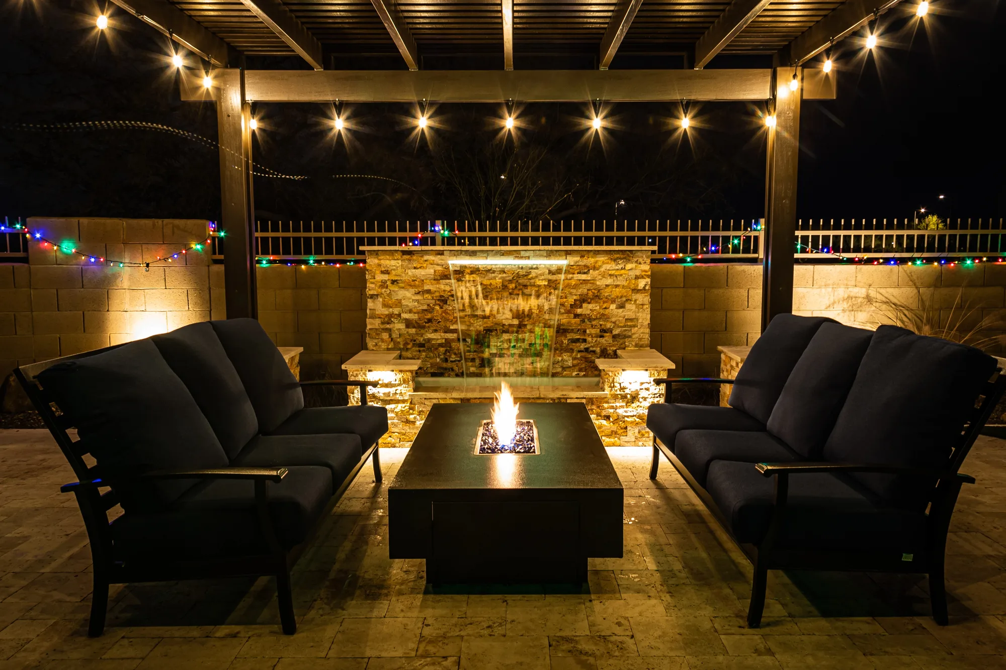 Covered entertaining area with lounges around a fire table under festoon lights