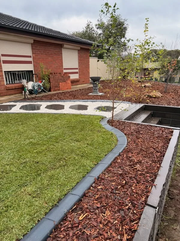 Curved garden bed edging with mulch and stepping stones