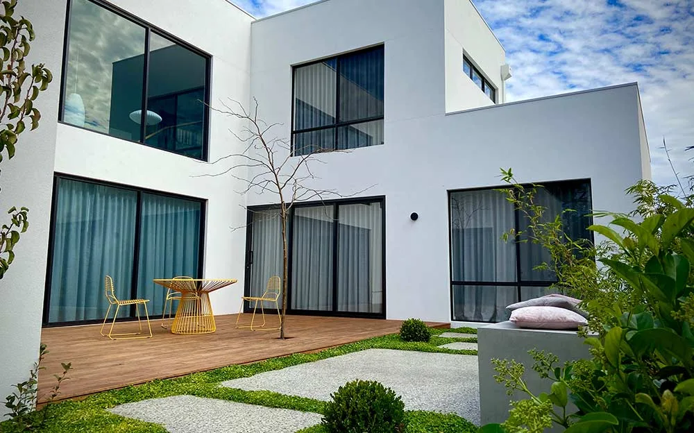 Contemporary white home with a timber deck, lawn pavers and garden planting