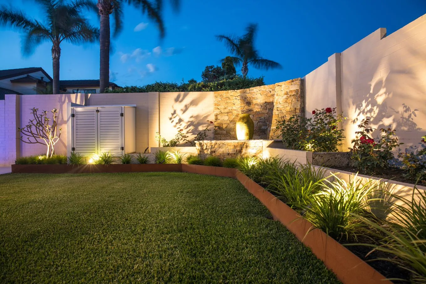 Landscaped backyard with lawn, corten steel edging and feature lighting at dusk