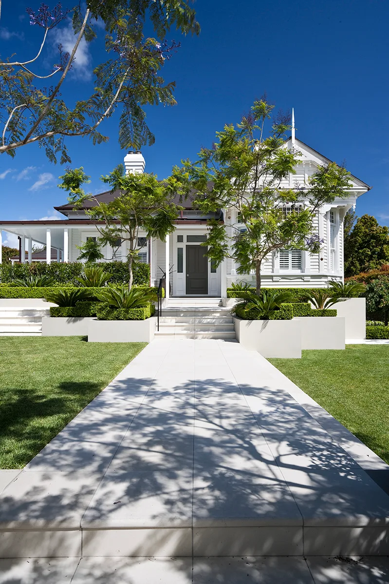 Formal front garden with a wide path, clipped hedges and lawn leading to a weatherboard home